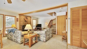A living room with a fireplace, a sofa, a TV, and a staircase leading to another level.