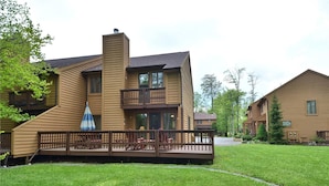 A two-story wooden cabin with a balcony, a deck with chairs, and a well-maintained lawn.