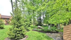 A well-maintained garden with various trees, a stone pathway, and a wooden deck.