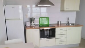 A compact kitchen with white cabinets, a stainless steel range hood, a sink, and a dining area with a table and chairs.