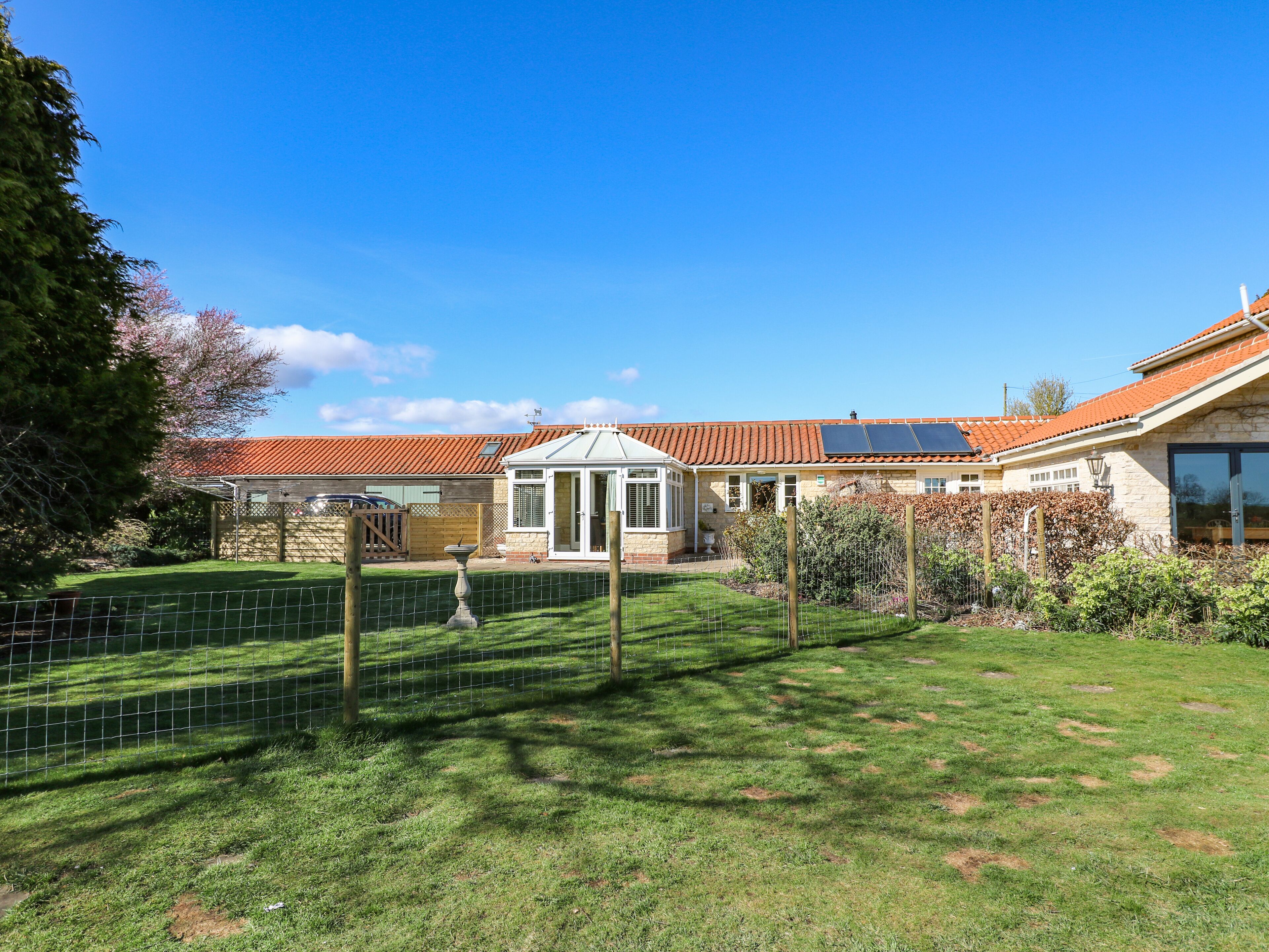 Een huis met een overdekte patio, een omheinde achtertuin en een zonnepaneel op het dak.