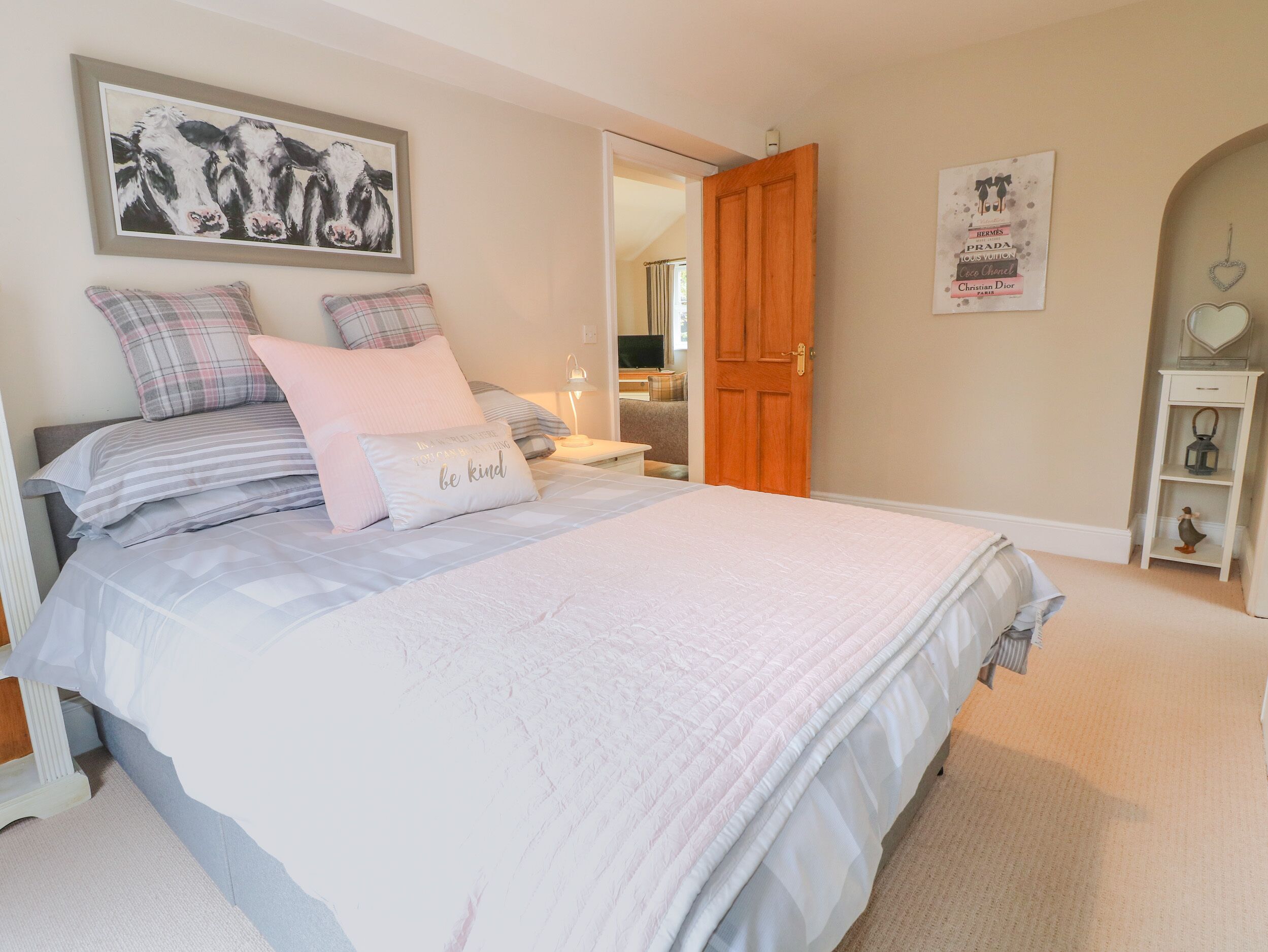 A bedroom with a bed, pillows, a framed artwork, a wooden door, and a shelf with decorative items.
