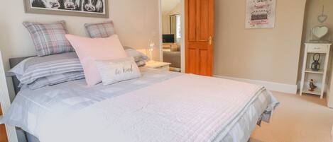 A bedroom with a bed, pillows, a framed artwork, a wooden door, and a shelf with decorative items.
