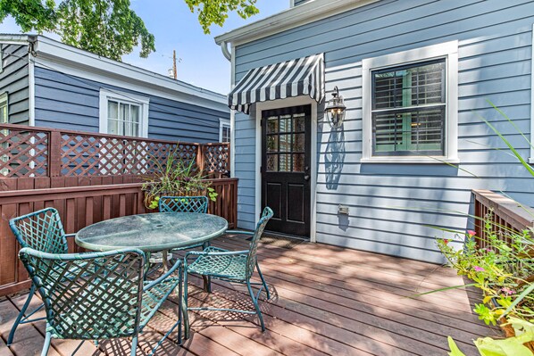 A blue house with a wooden deck, a black door, and a small garden area with a table and chairs. - Enchanting Home w/ Luxurious Kitchen and Serene Courtyard by Lucky Savannah (Savannah)