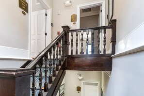 A wooden staircase with a dark balustrade, white walls, and a door with a plaque.