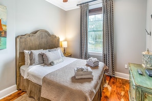 A neatly made bed with a wooden headboard, a bedside lamp, and a window with patterned curtains.