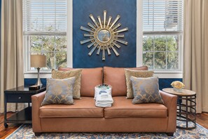Een bruine leren bank met gekleurde kussens, een decoratieve spiegel en een klein tafeltje met een lamp.