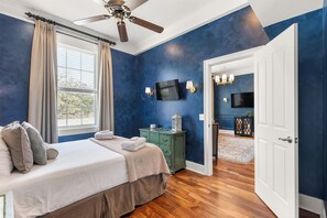 A bedroom with a bed, a ceiling fan, a television, and a green dresser.