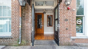 A brick building entrance with a wooden door, a small porch, and a window with a bicycle outside. - Charming Downtown Studio One Block From The River by Lucky Savannah (Savannah)