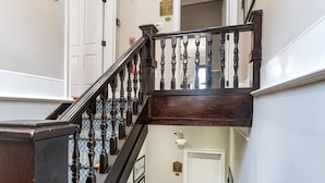 A wooden staircase with a dark balustrade, white walls, and a door with a plaque. - Charming Downtown Studio One Block From The River by Lucky Savannah (Savannah)