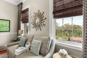 A well-lit room with a sofa, a decorative mirror, and a view of trees through a window.