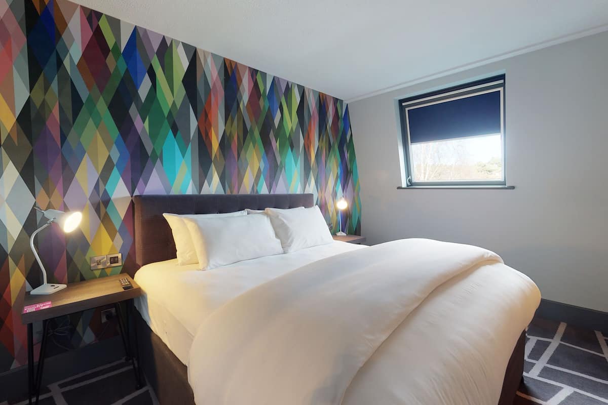 A neatly made bed with white linens, a modern headboard, and a colorful geometric-patterned wall.