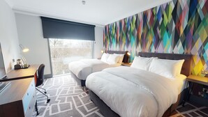 A hotel room with two beds, a desk, and a large window. - Village Hotel Bracknell (Bracknell)