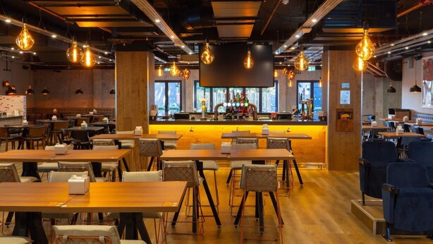 A modern restaurant interior with wooden tables and chairs, a bar area, and pendant lighting. - Village Hotel Bracknell (Bracknell)