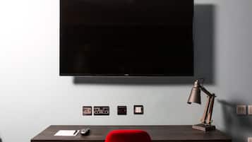 Una habitación moderna con una televisión de pantalla plana en la pared, un escritorio con una lámpara y una silla roja.