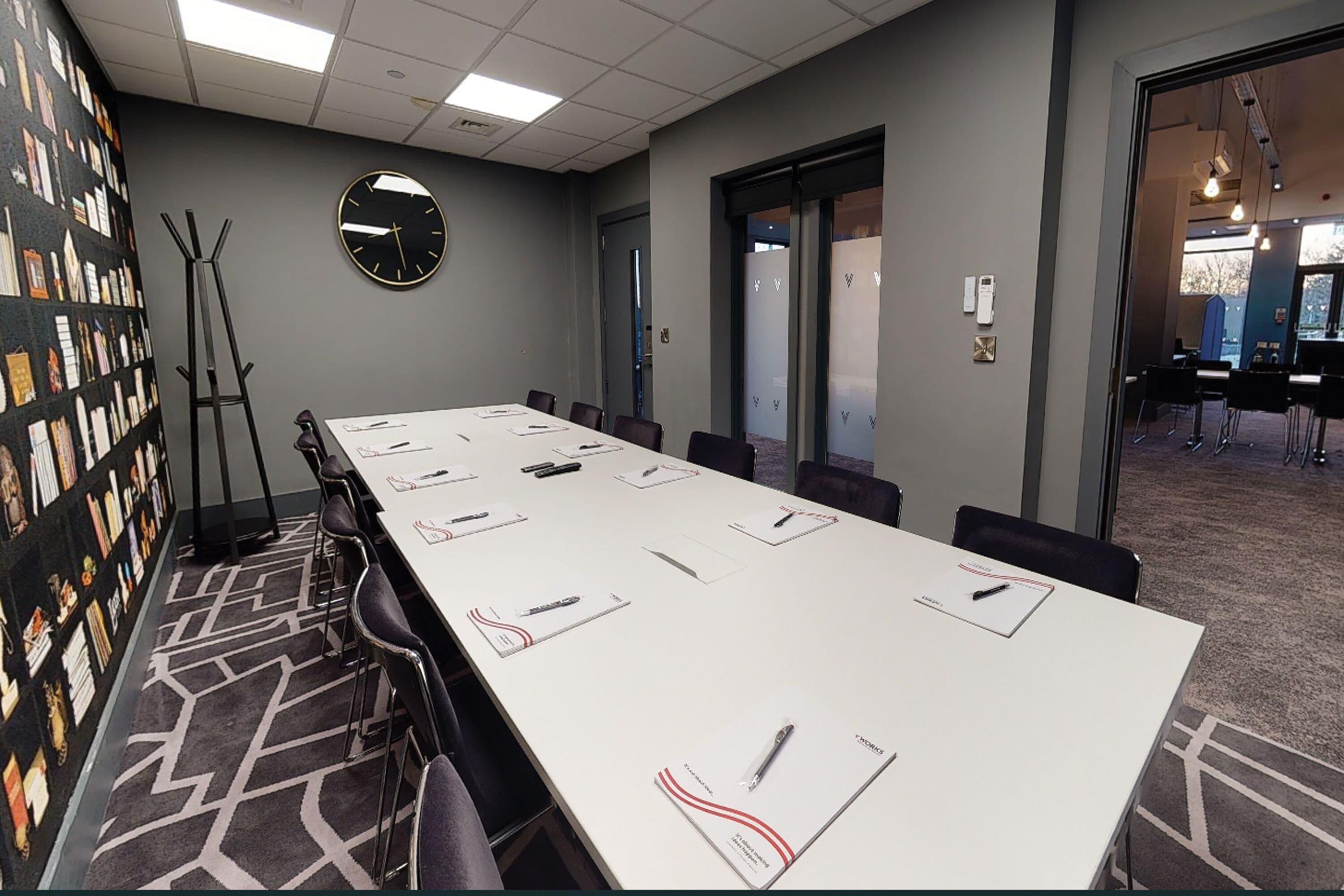 Un salón de conferencias con una larga mesa, sillas, un reloj y una estantería con diversos objetos.