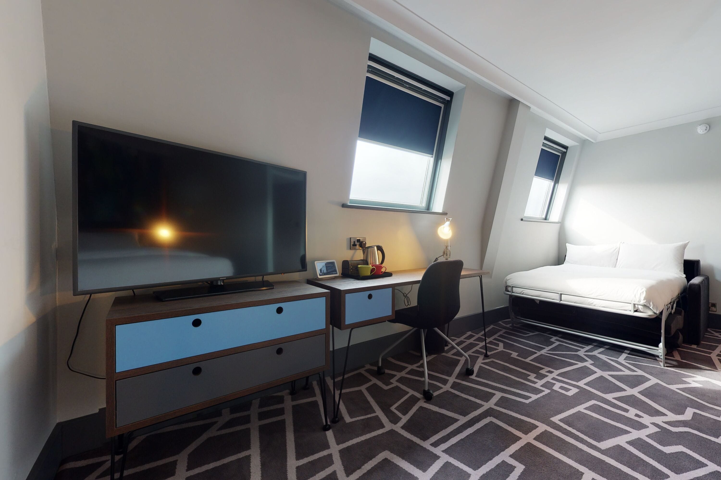 A hotel room with a bed, a desk with a computer, a TV, and a window.