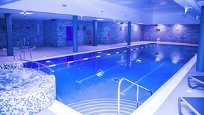 An indoor swimming pool with a tiled edge, a hot tub, and a stone wall backdrop. - Village Hotel Bracknell (Bracknell)