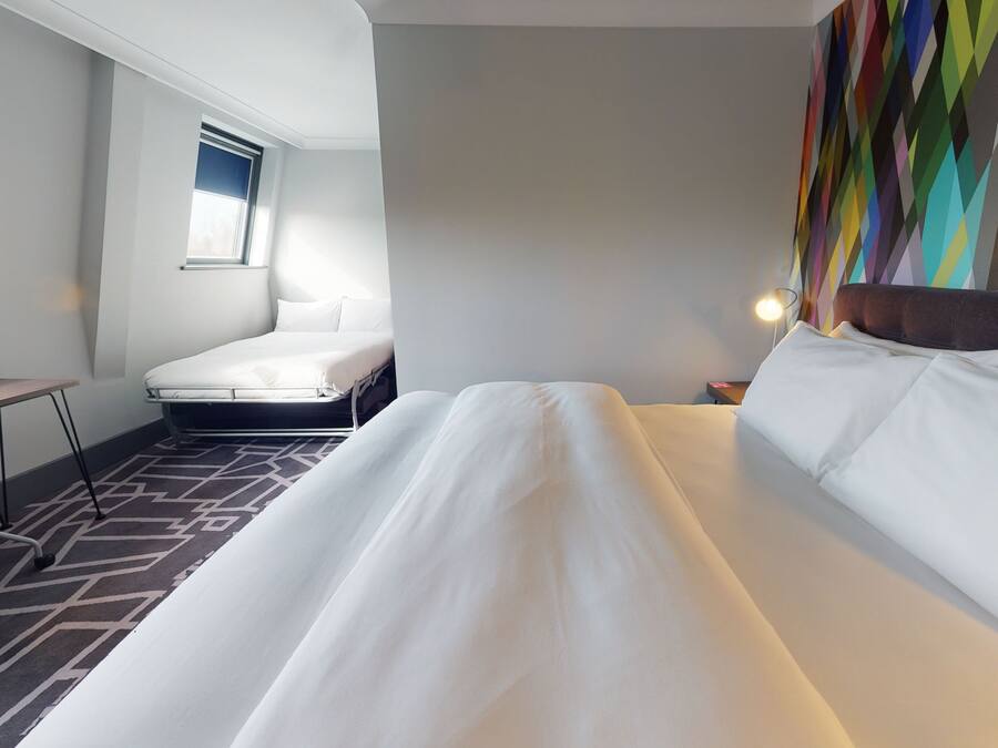A hotel room with a large bed, a desk, and a window.