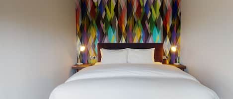 A hotel room with a large bed, a colorful geometric wall design, and two bedside lamps.