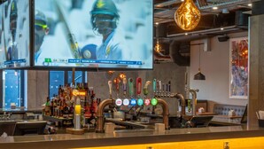 A bar area with multiple taps, a television displaying a sports event, and seating. - Village Hotel Bracknell (Bracknell)