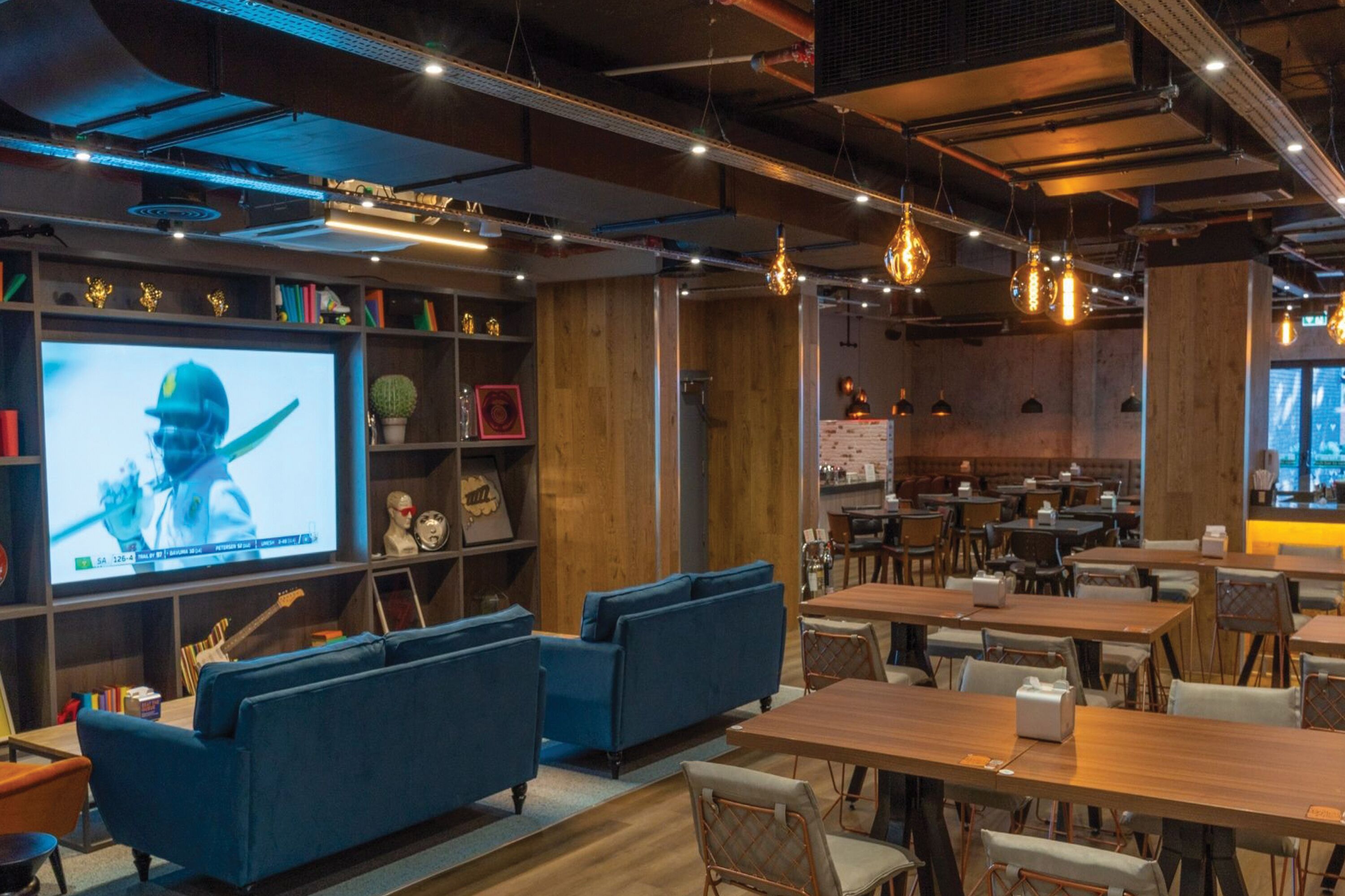 A modern restaurant with wooden walls, blue sofas, and hanging lights.