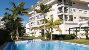 Ein mehrstöckiges Hotel mit Balkonen, einem Schwimmbad und Palmen.