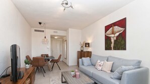 Ein modernes Wohnzimmer mit einem grauen Sofa, einem Holztisch, einem Fernseher auf einem Holzmöbelstück, einem Essbereich mit Tisch und Stühlen und einem Bild an der Wand.