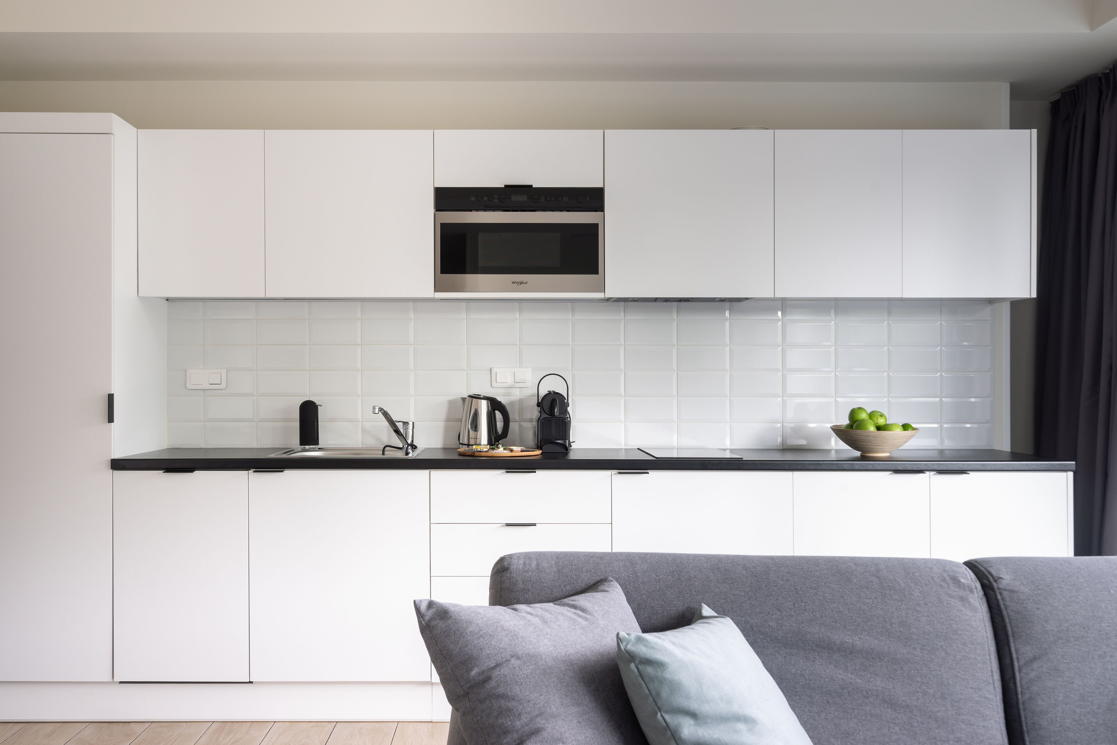 Una cocina moderna con armarios blancos, horno integrado y encimera negra.