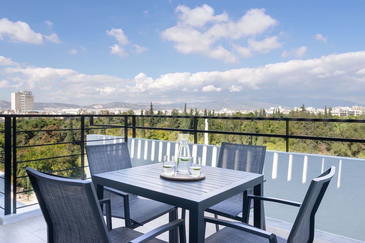 A balcony with a table and chairs, a pitcher, and glasses.