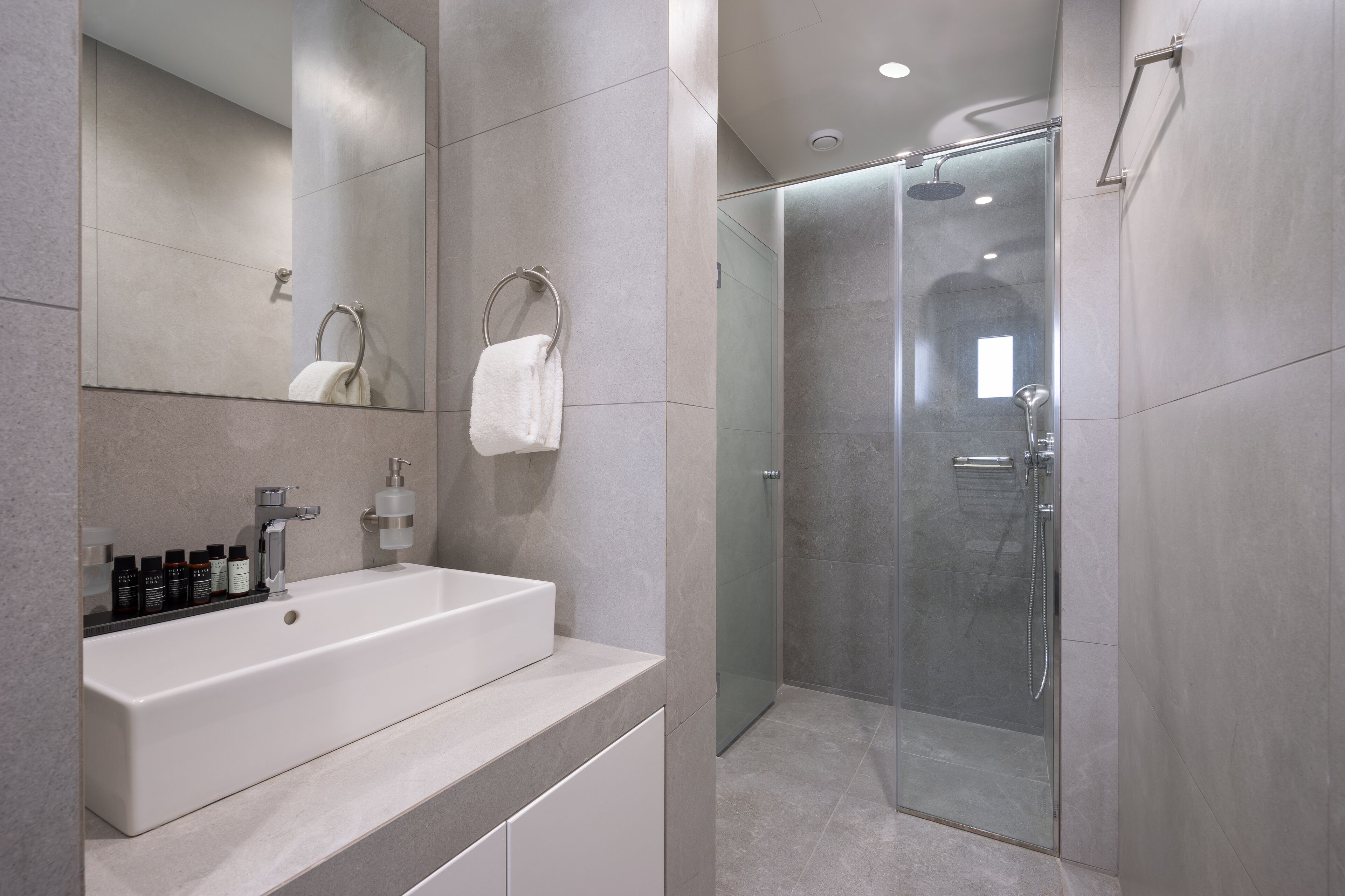 A modern bathroom with a large mirror, a white sink, and a glass-enclosed shower.