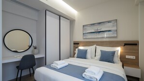 Una habitación de hotel moderna con una cama grande, mesitas de noche, un escritorio con una silla, un espejo redondo y un cuadro en la pared.