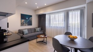 Una sala de estar moderna con un sofá, una mesa de comedor con un frutero y un ventanal con cortinas.