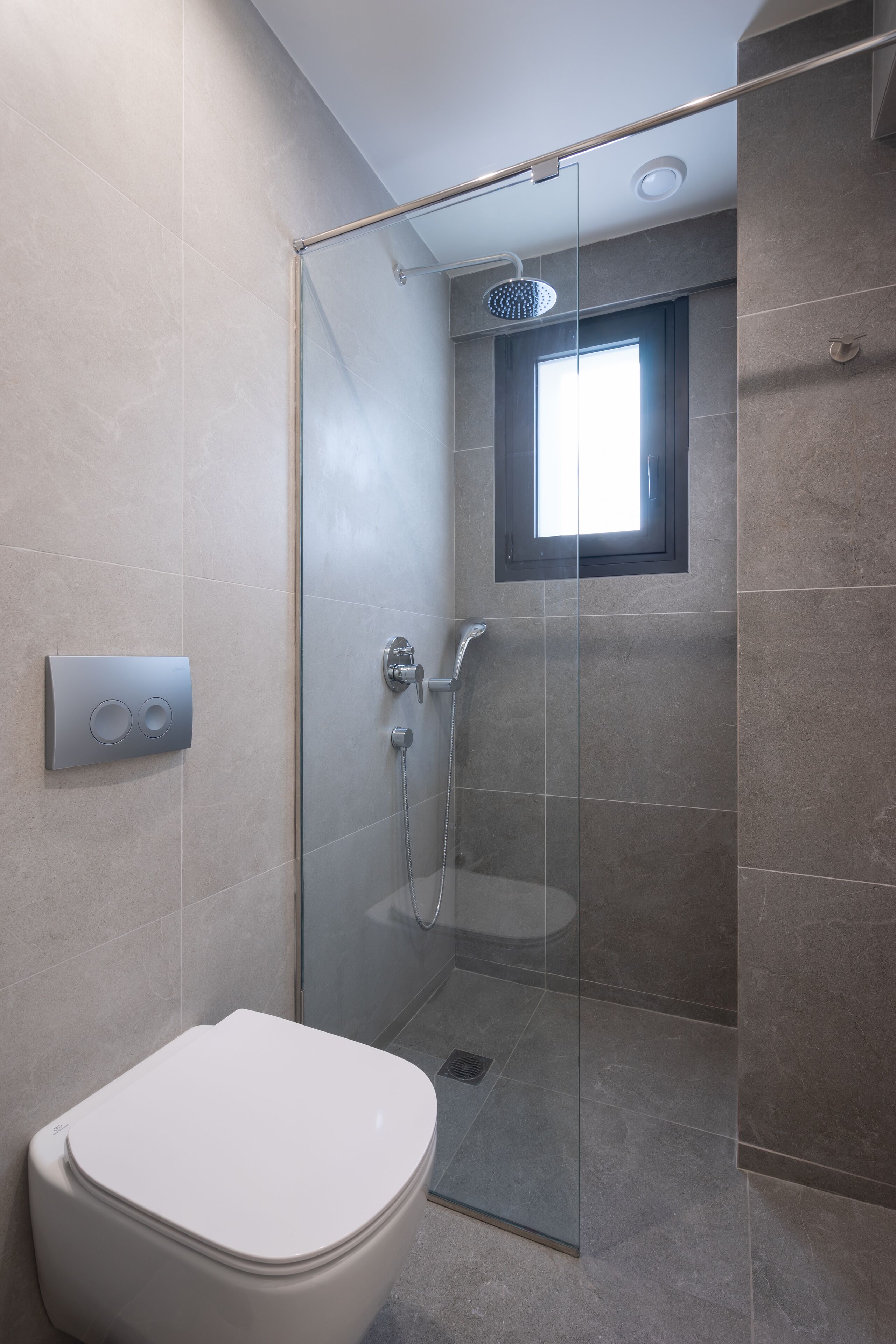 A modern bathroom with a glass-enclosed shower, a toilet, and a window providing natural light.