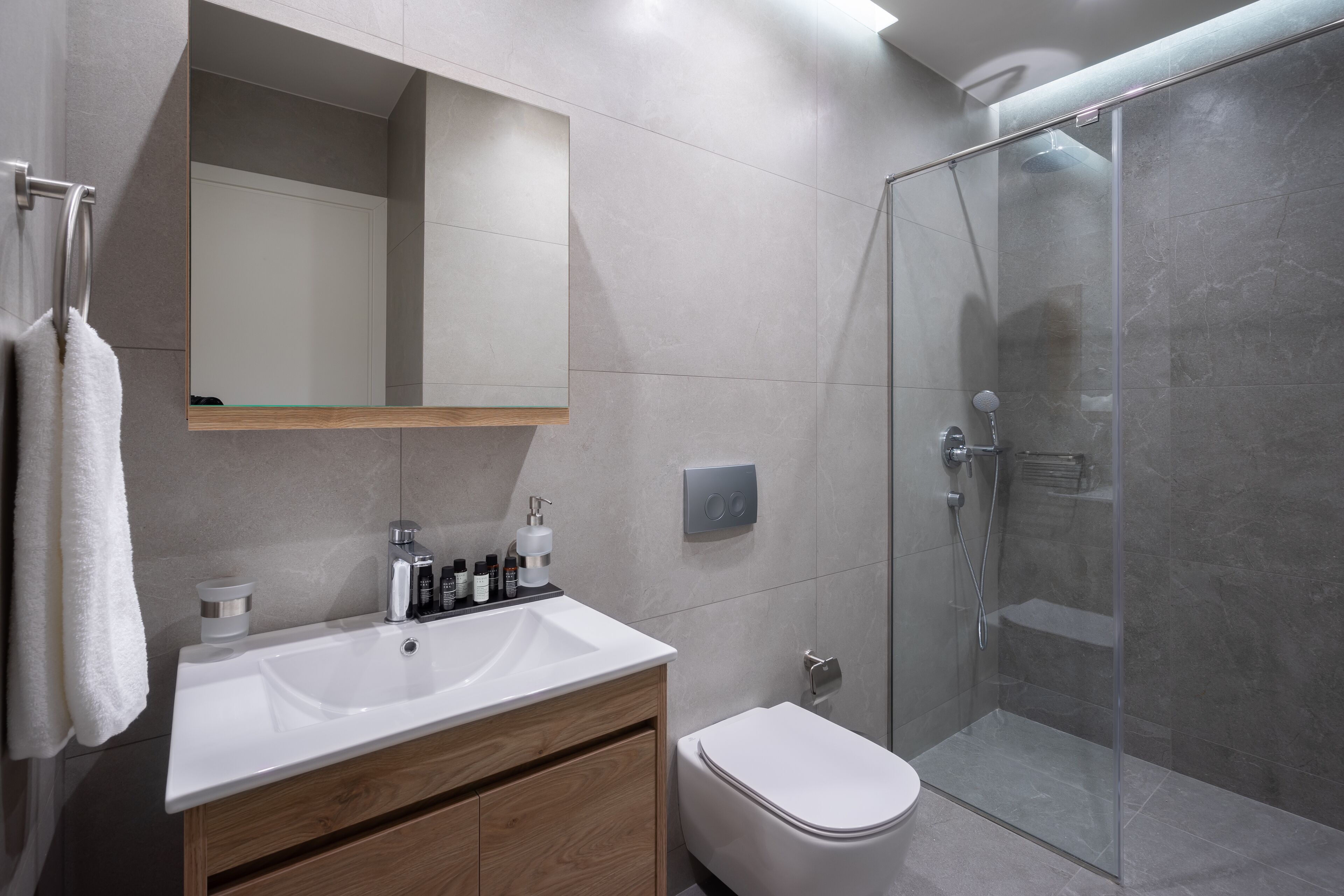 A modern bathroom with a glass shower enclosure, a white sink, and a wooden vanity.