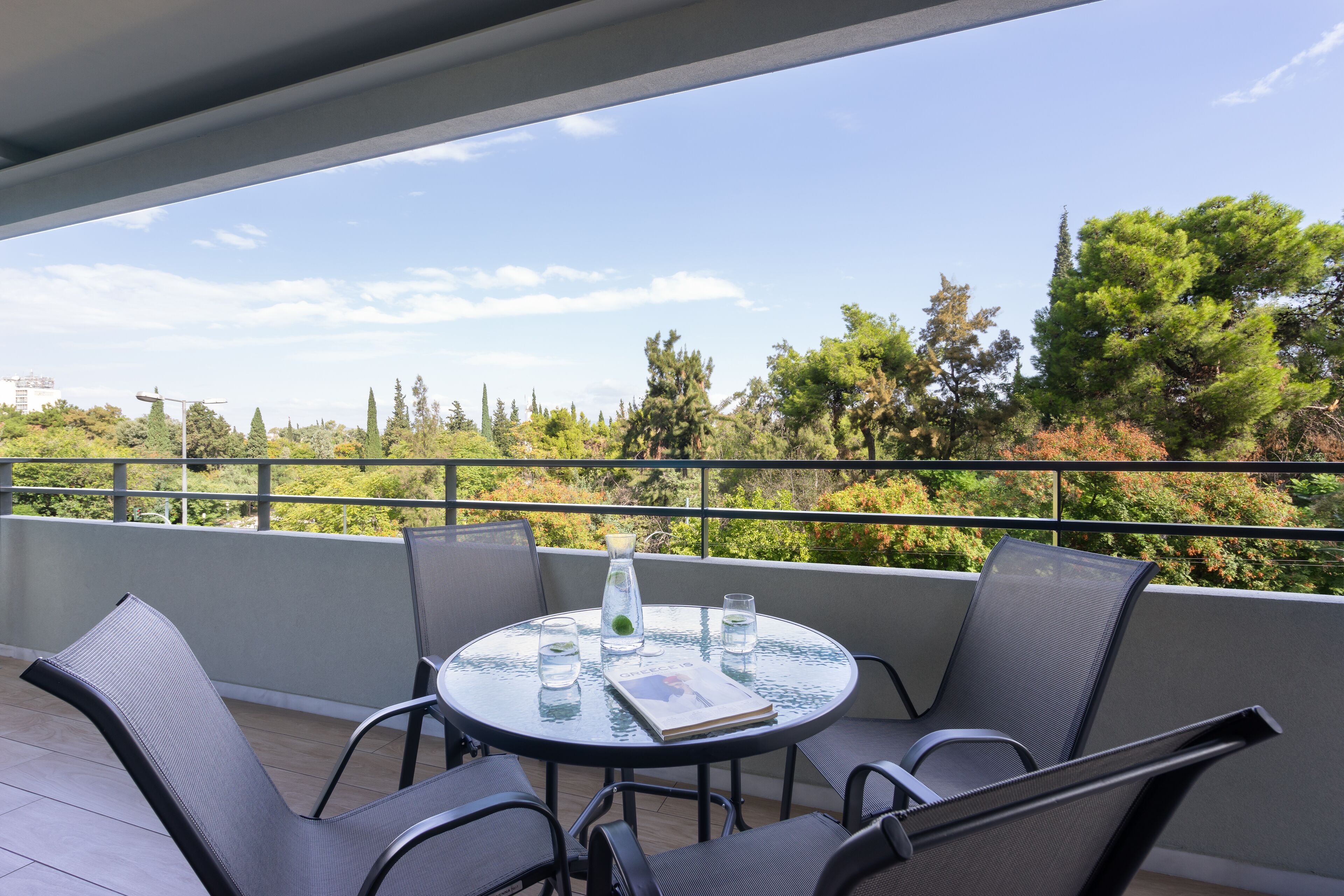 A round table with chairs on a balcony, a book, and a glass pitcher.