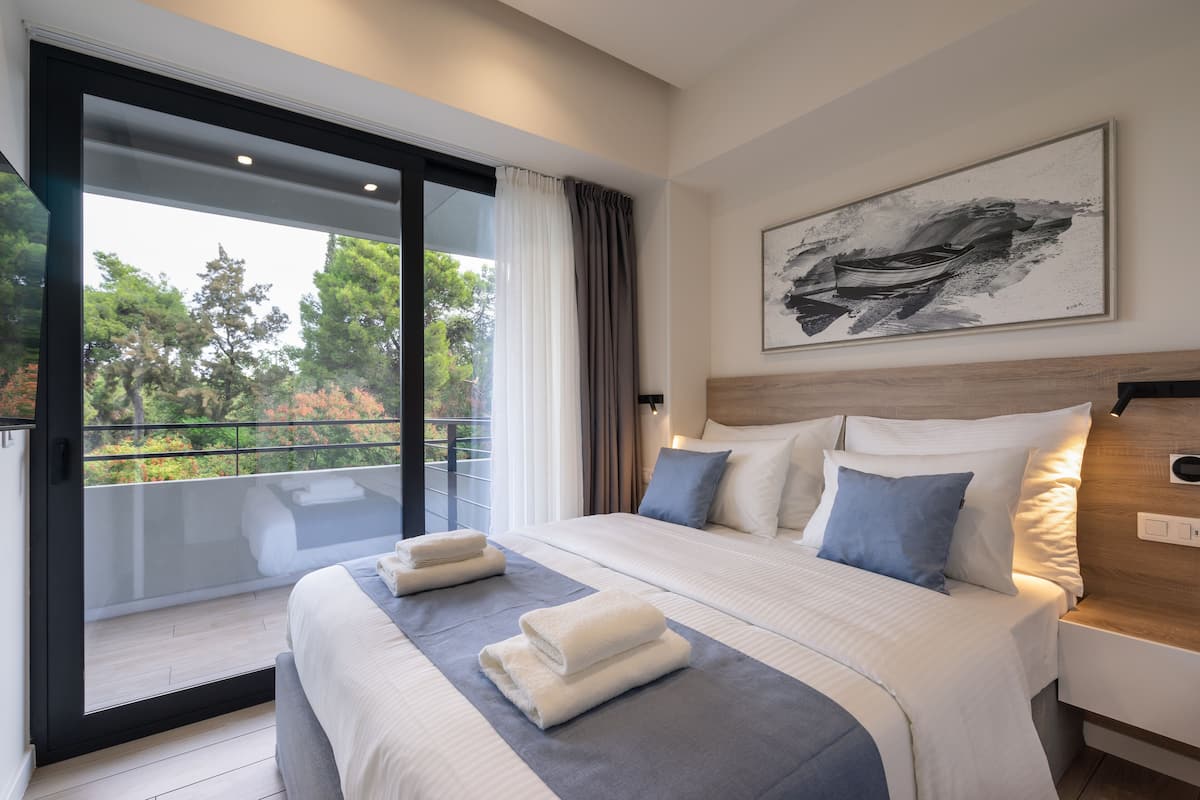 A modern hotel room with a large bed, a view of the outdoors, and a painting on the wall.