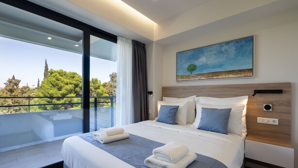 Una habitación de hotel moderna con una cama grande, un cuadro y un balcón con vistas a árboles.
