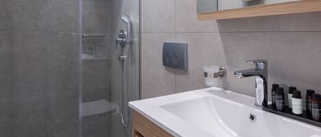 Ein modernes Badezimmer mit einer Duschkabine aus Glas, einem weißen Waschbecken und einem Holzlagerfläschchen.