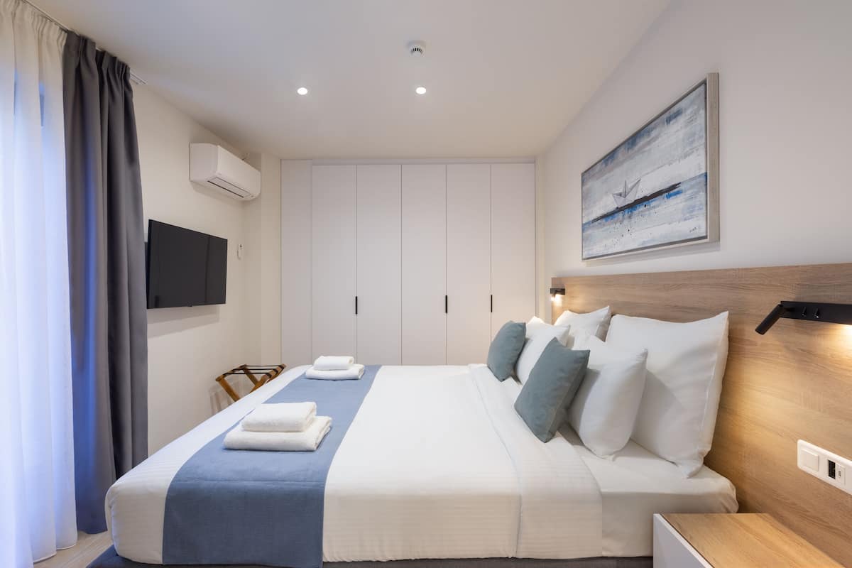 A modern hotel room with a large bed, a flat-screen TV, a wooden headboard, and a painting on the wall.