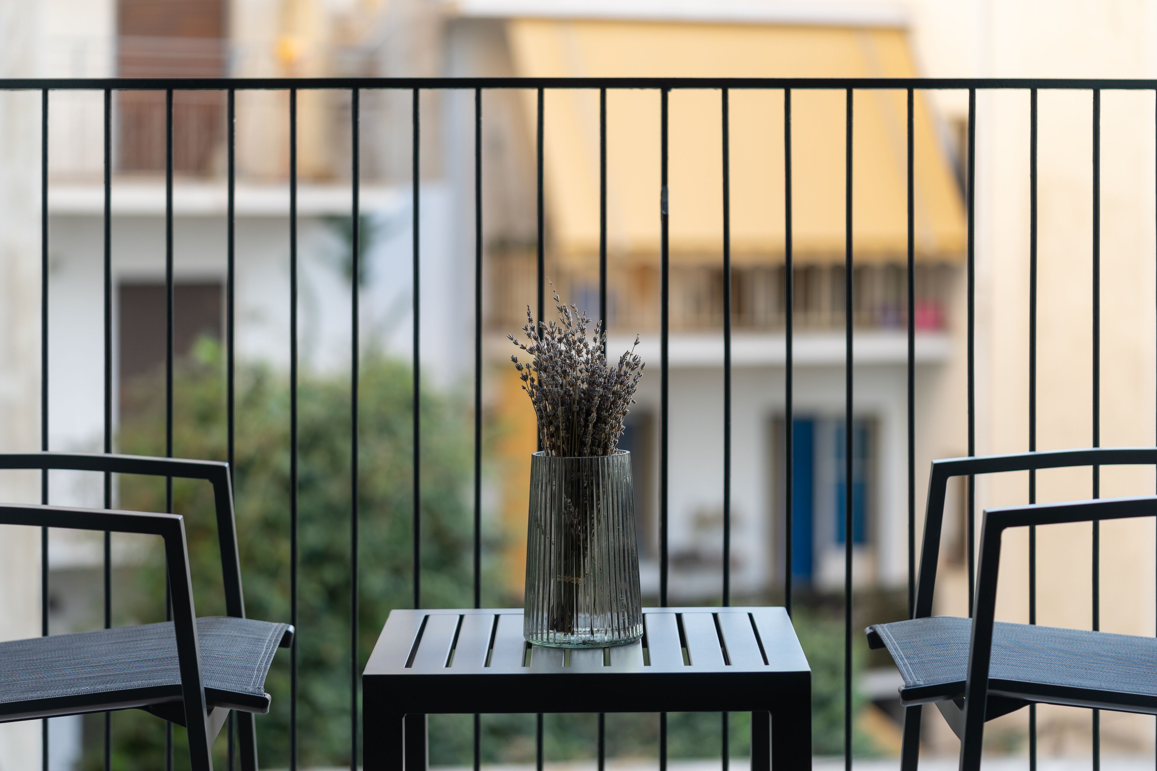 A balcony with two chairs and a vase of lavender.