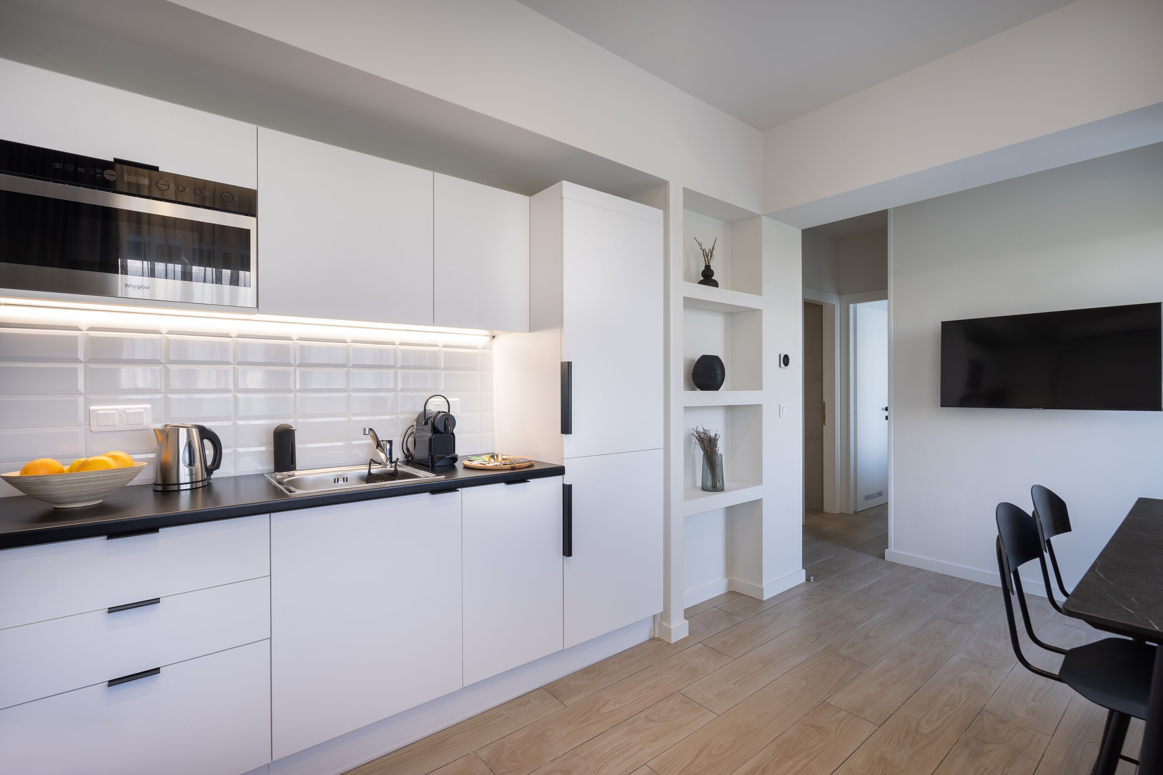 Eine moderne Küche mit weißen Schränken, einer schwarzen Arbeitsplatte und einem eingebauten Backofen. Es gibt einen Essbereich mit Tisch und Stühlen.