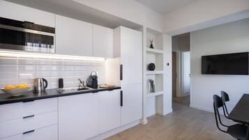 Eine moderne Küche mit weißen Schränken, einer schwarzen Arbeitsplatte und einem eingebauten Backofen. Es gibt einen Essbereich mit Tisch und Stühlen.