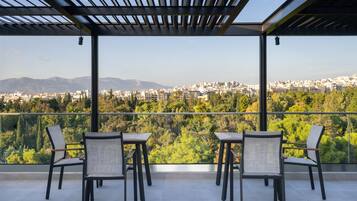 A terrace with four chairs and tables, offering a view of a cityscape and mountains.