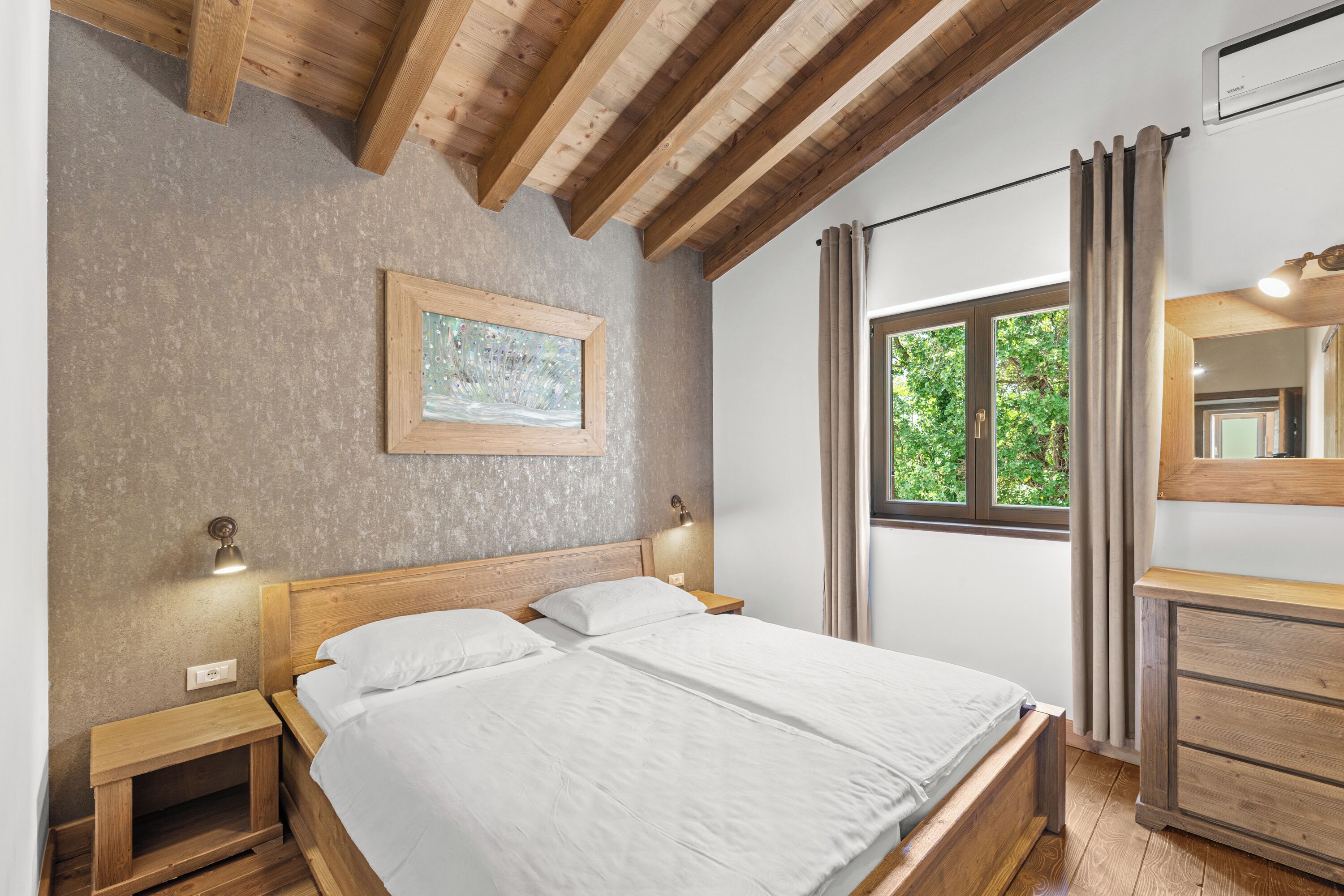 Un dormitorio con una cama de madera, mesitas de noche, un aparador, un cuadro enmarcado en la pared, una ventana con cortinas y un cómoda de madera.