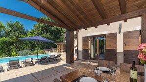 An outdoor patio with a pool, wooden furniture, and a dining table set for two with wine glasses and a bottle. - Villa Dali with whirlpool, sauna and 5 bedrooms (Svetvinčenat)
