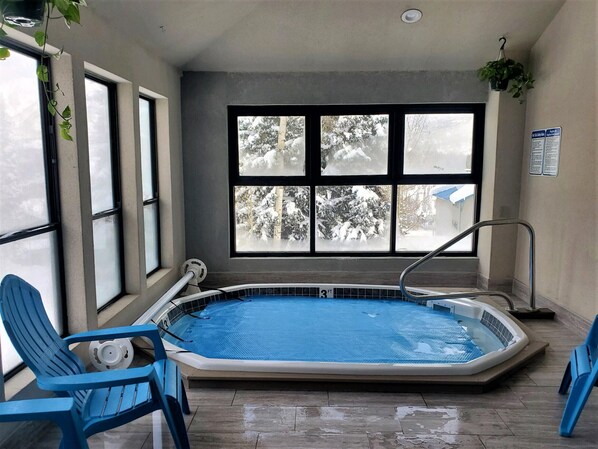 A small indoor swimming pool with a view of snowy trees through large windows.
