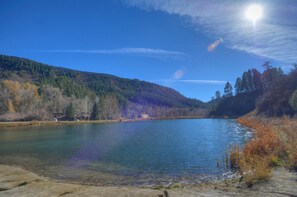 A serene lake surrounded by forested hills, with clear skies and a bright sun. - River Front Cabin on 1 acre  - 14 Minutes to Downtown Durango (Durango)