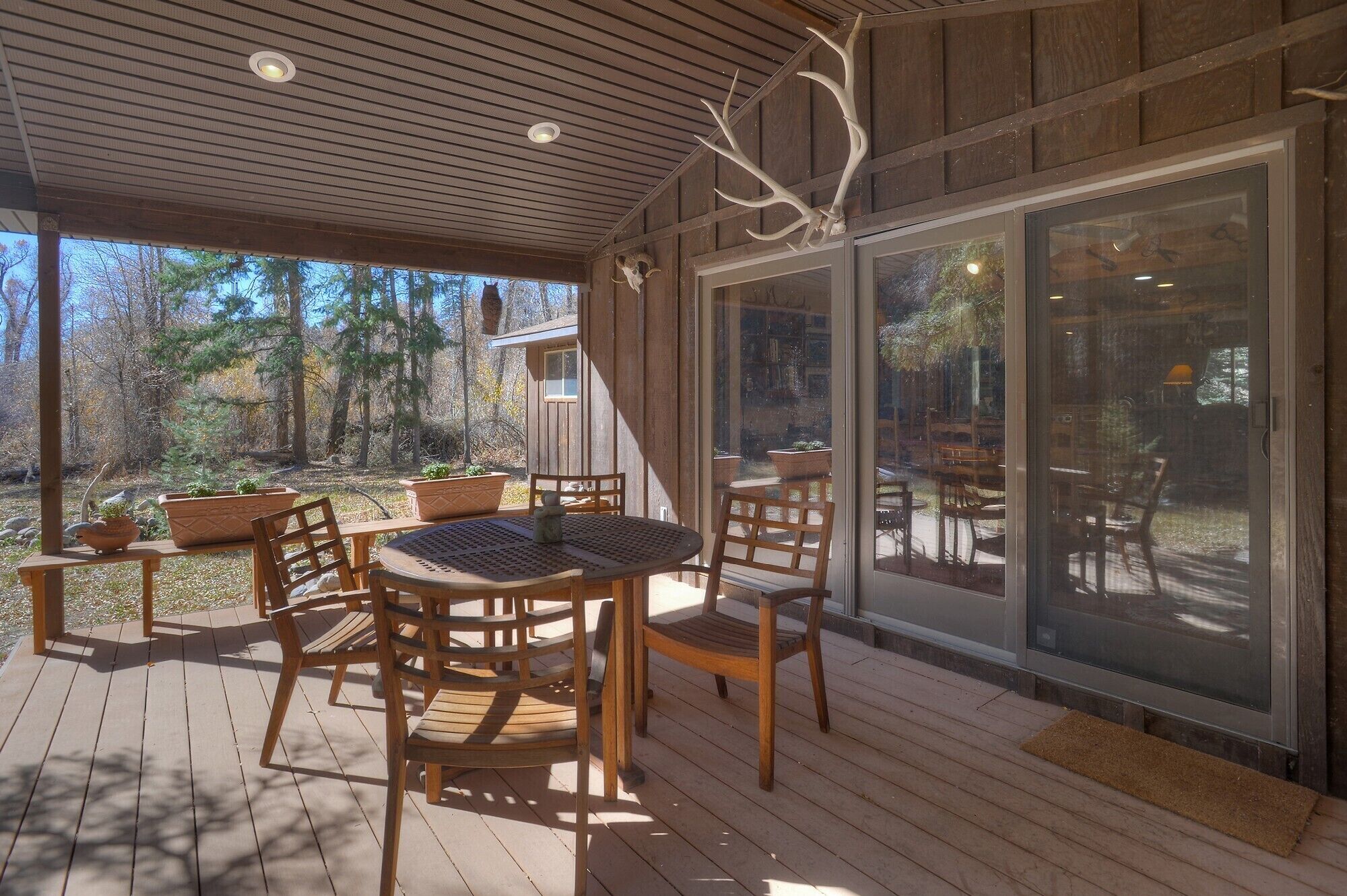 Eine Terrasse im Freien mit Holzmöbeln und einer Glastür, die in einen Garten führt.
