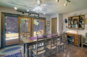 A rustic wooden dining area with a large table and chairs, a ceiling fan, and a bookshelf with various items.